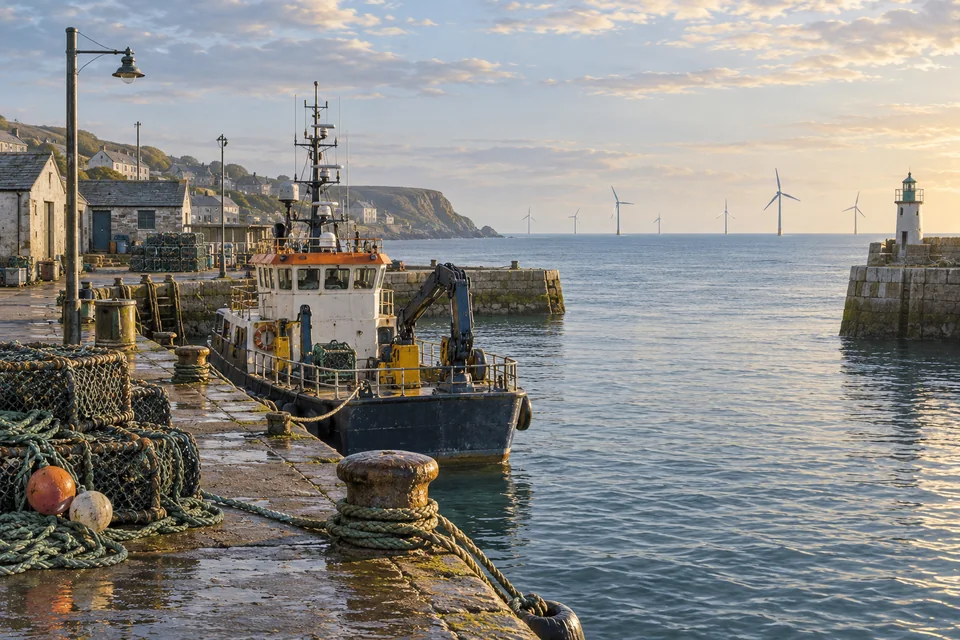 A maintenance vessel sits in a harbour with distant wind turbines.